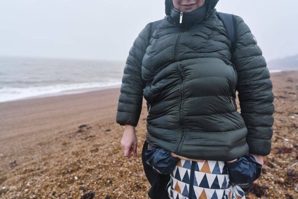 Autistic child hiding under his mothers coat from the wind and rain on the beach during a family photo session