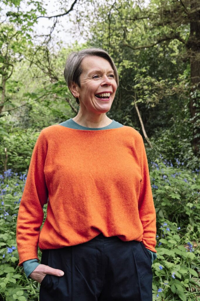 Woman wearing an orange sweater which contrast beautifully with the green background in this professional headshot. 
