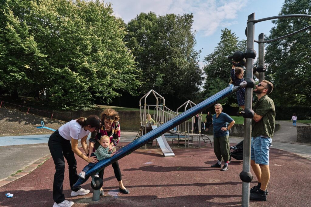 Unposed family portrait outdoors in London playground with parents, grandmother, aunt and children playing together