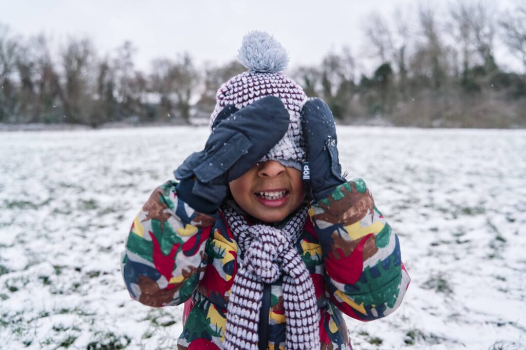 Candid moment of child’s adjusting winter hat during natural family photography session in London